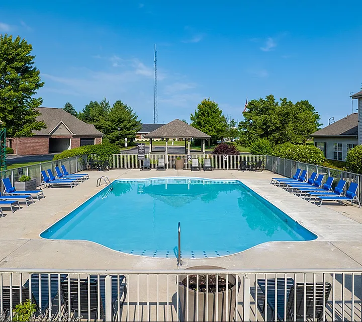 Inviting outdoor pool surrounded by blue lounge chairs, perfect for relaxation, set in a sunny and lush community area.