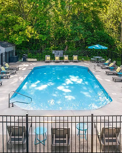 Inviting outdoor pool area surrounded by lush greenery, featuring comfortable lounge chairs and vibrant umbrellas for a perfect relaxation spot.