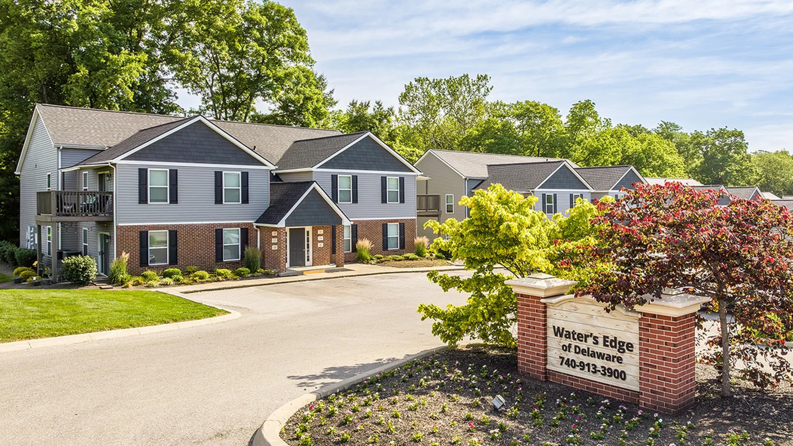 Inviting suburban complex surrounded by lush greenery, showcasing modern two-story brick and siding apartment buildings at Water's Edge of Delaware.