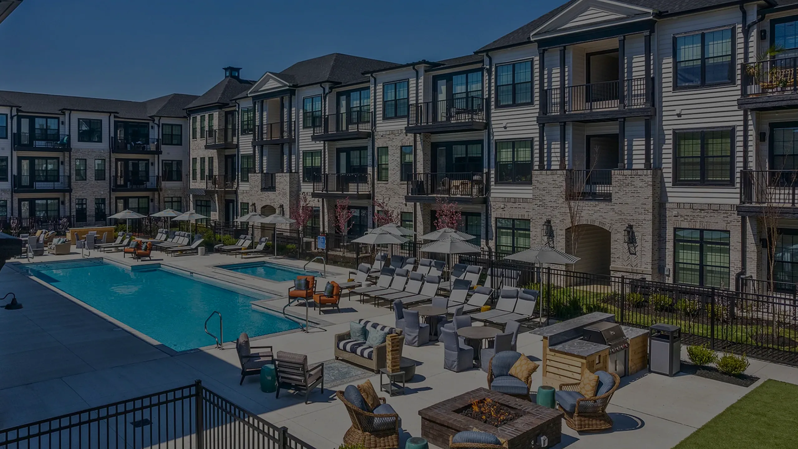 Modern apartment complex with luxurious outdoor pool, stylish lounge seating, and elegant architecture bathed in sunlight.