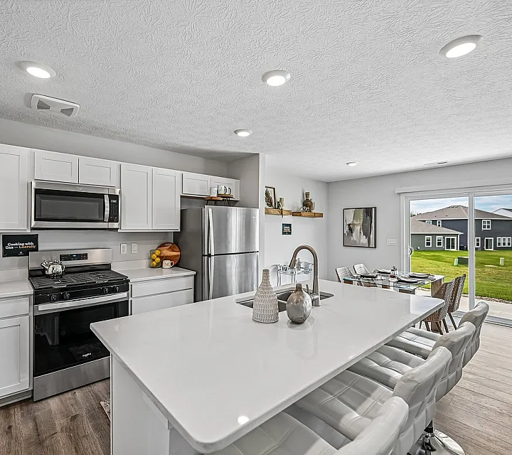 Modern kitchen with sleek white cabinetry, stainless steel appliances, and a stylish island leading to a sunlit dining area with garden views.