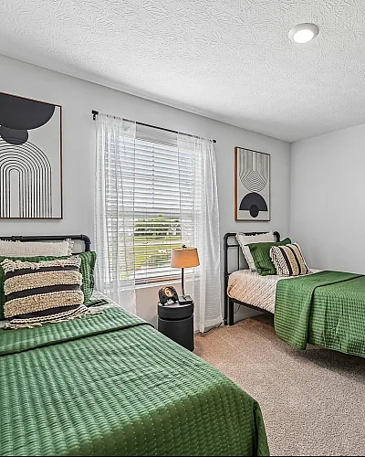 Inviting bedroom with two twin beds in fresh green linens, modern wall art, and ample natural light through a large window.