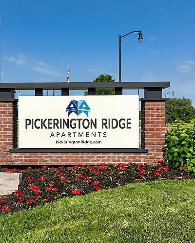 Inviting entrance sign for Pickerington Ridge Apartments surrounded by lush greenery and vibrant flowers, set against a clear blue sky.