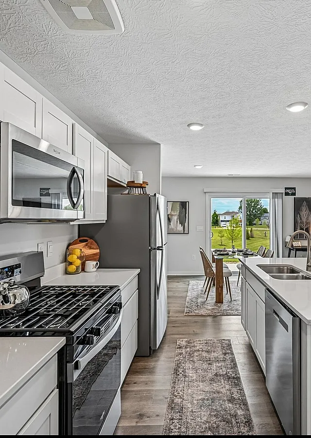 Modern open-plan kitchen and living area featuring sleek white cabinets, stainless steel appliances, and a large island counter leading to a cozy, bright living room with comfortable seating and garden views.