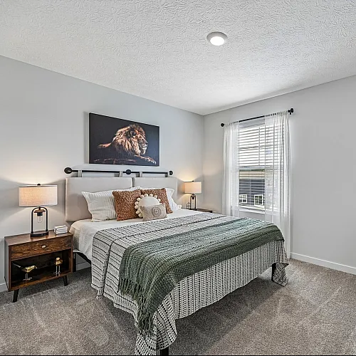 Chic bedroom with elegant decor featuring a plush bed, cozy chair, large wall clock, and stylish lion artwork, filled with natural light.