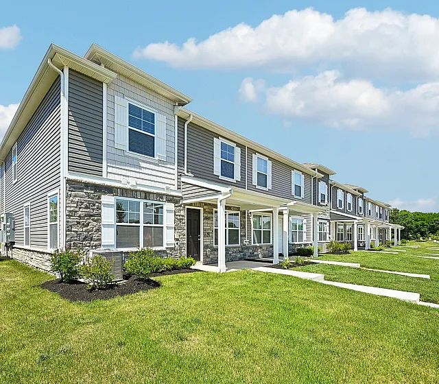 Charming townhouse row with modern siding, lush green lawns, and bright windows under a clear blue sky.