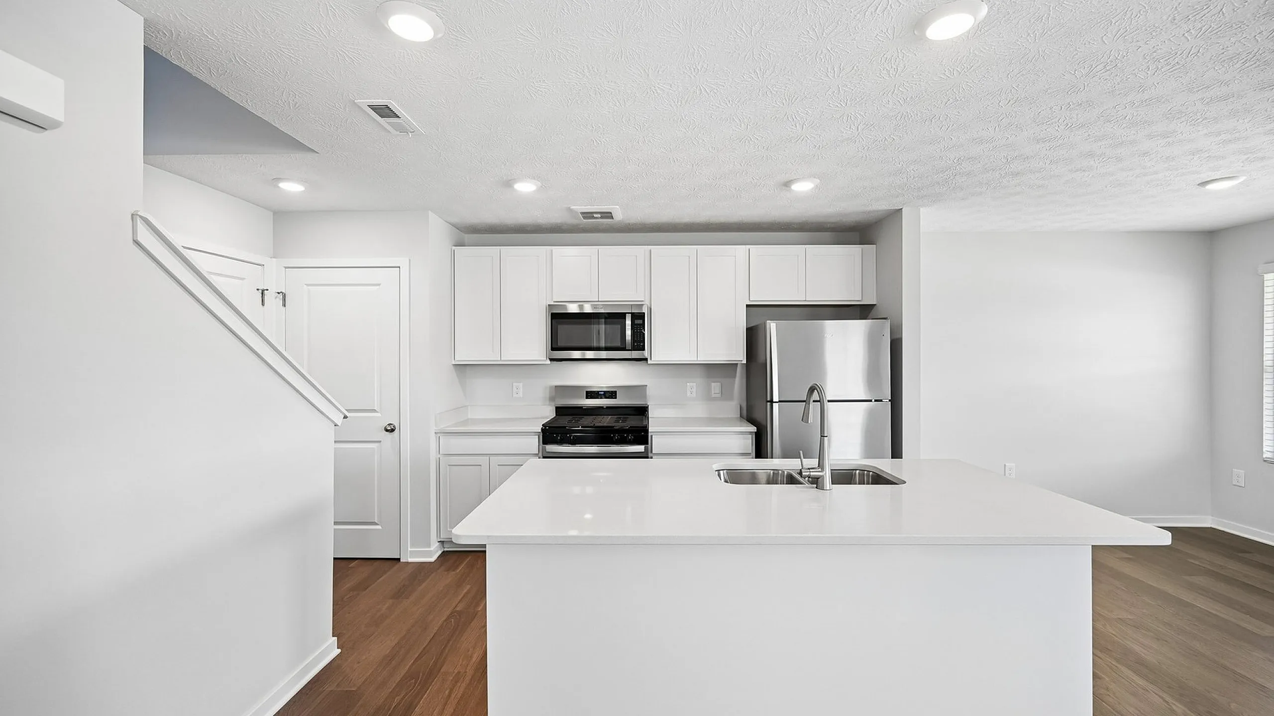 Modern kitchen with pristine white cabinets, a sleek island with dual sinks, stainless steel appliances, and warm wood flooring for a contemporary living space.