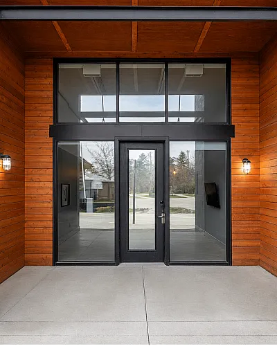 Modern apartment entrance with sleek black frame door and warm wood paneling, exuding contemporary elegance.