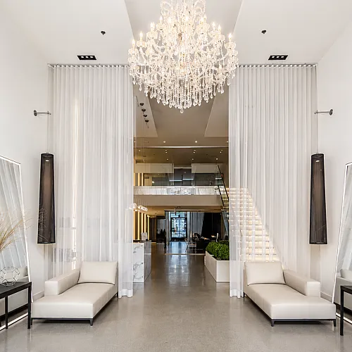 Luxurious apartment lobby featuring a grand chandelier, elegant white sofas, and modern decor with a stunning staircase.
