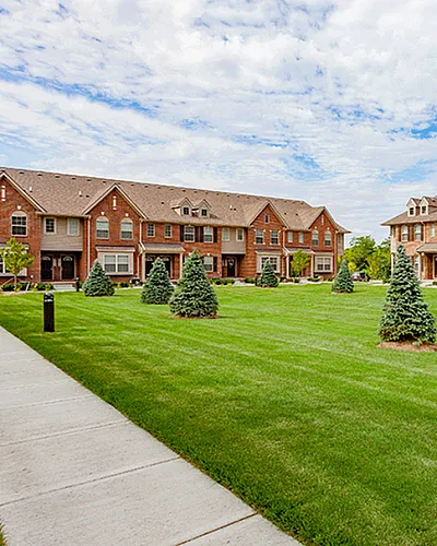 Charming townhouse community with red brick exteriors, manicured lawns, and lush greenery under a bright blue sky.