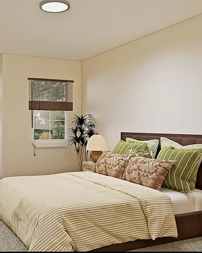 Charming bedroom with tasteful decor featuring a cozy armchair, modern striped bedding, and large windows overlooking lush greenery.