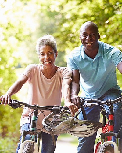 Joyful couple riding bicycles on a scenic forest trail, enjoying the fresh air and vibrant green surroundings.