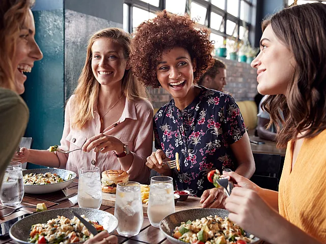 Group of friends joyfully dining together at a chic restaurant, sharing laughter and vibrant salads.