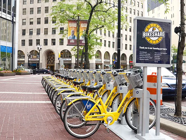 Vibrant urban bike-sharing station with a row of bright yellow bikes ready for use in a bustling city square.