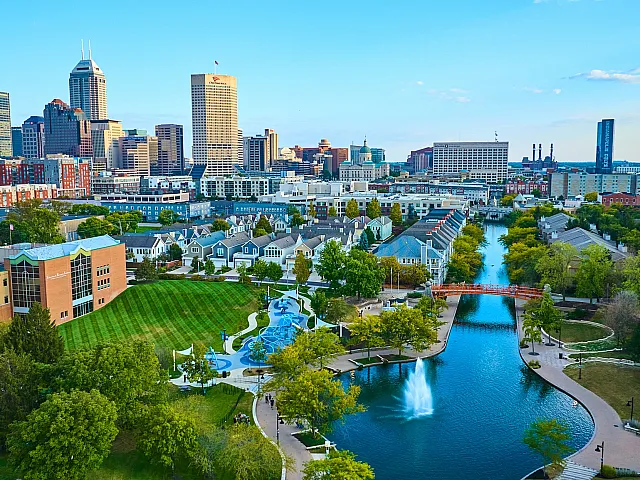 Vibrant urban scene showcasing a serene canal, lush green parks, and a dynamic city skyline under a bright blue sky.