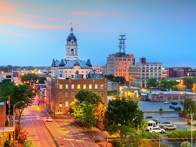 Charming cityscape of downtown Evansville at dusk featuring historic architecture, vibrant streetlights, and lush greenery.