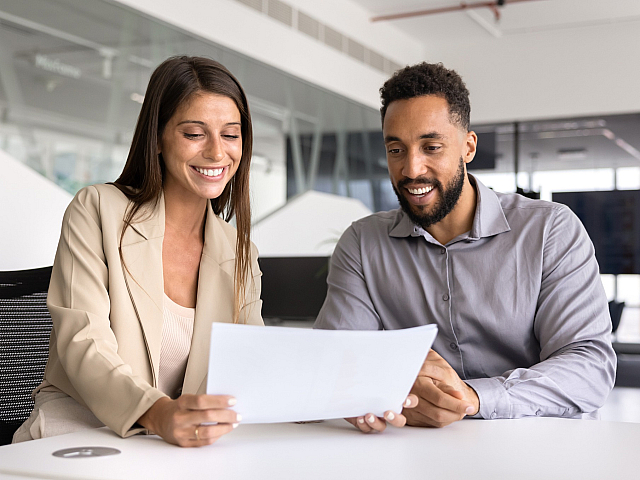 Two colleagues happily reviewing a document in a modern office setting, showcasing collaborative and positive work environment.