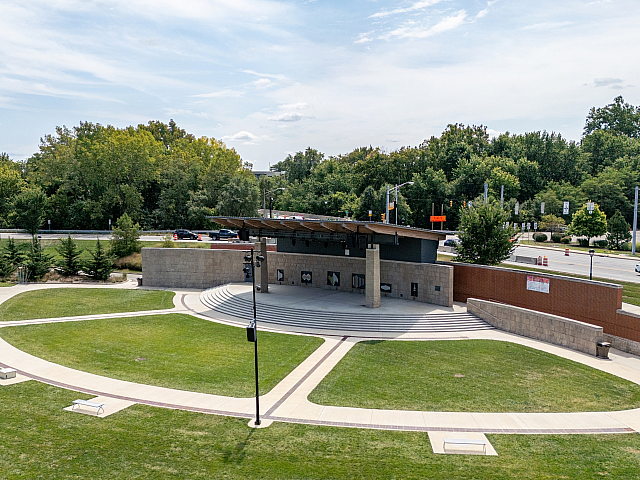 Charming outdoor amphitheater with lush green lawns, curved pathways, and a modern stage set against a backdrop of vibrant trees.