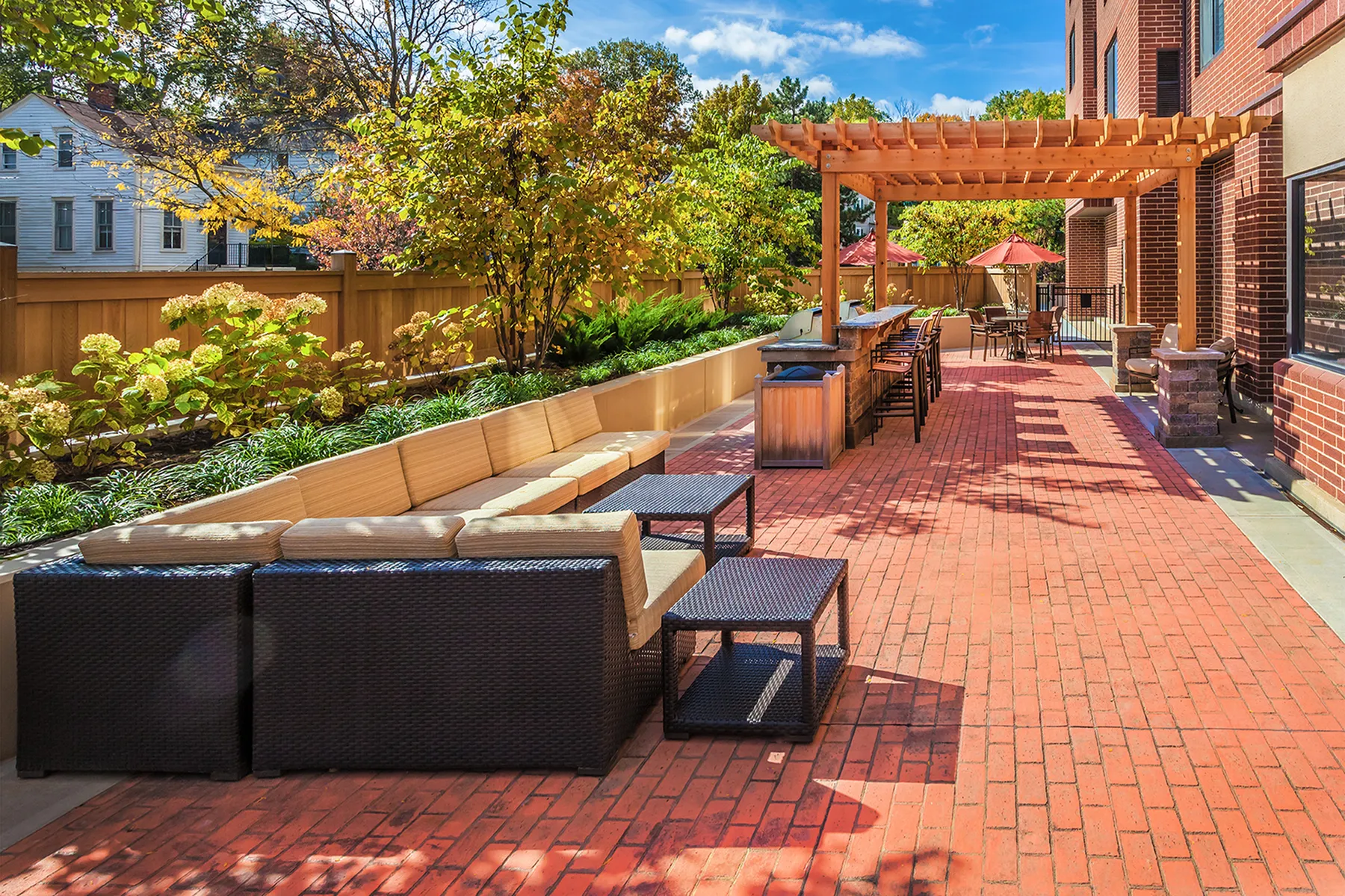 Charming outdoor patio with cozy seating, lush greenery, and a stylish pergola under a clear blue sky.