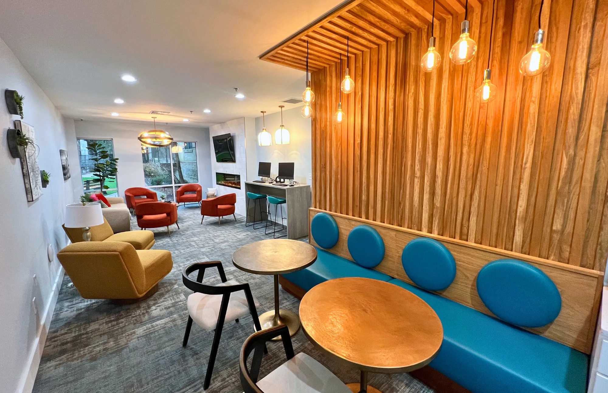 Modern communal space boasting vibrant seating, stylish wooden accents, and eye-catching pendant lighting for a cozy ambiance.