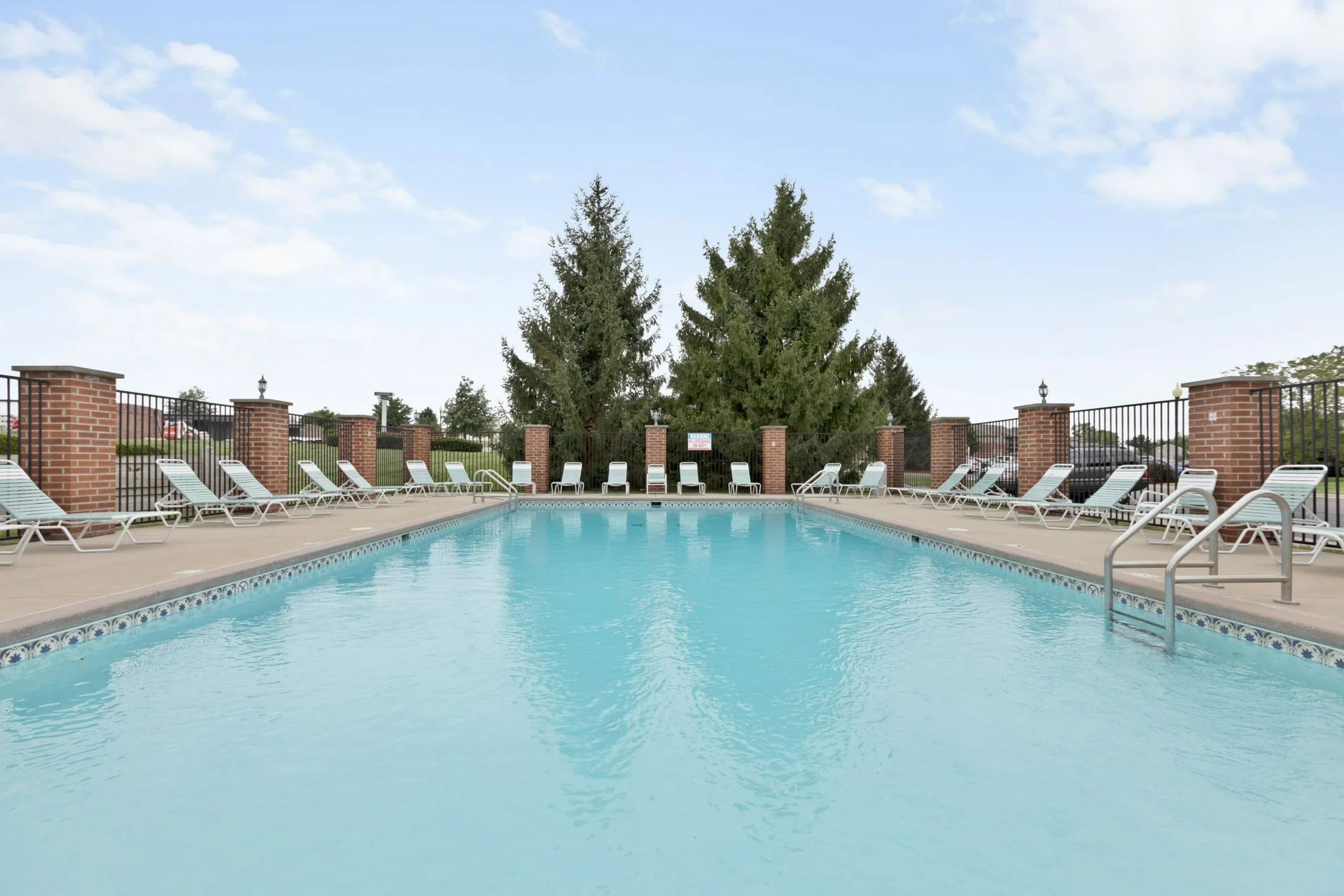 Inviting outdoor pool area with crystal-clear water, surrounded by elegant sun loungers and lush greenery, perfect for relaxation and leisure.