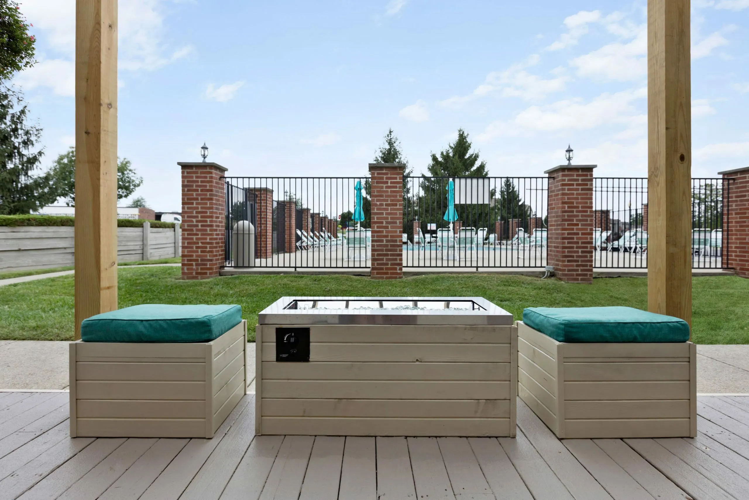 Chic outdoor patio with stylish seating and modern fire pit, overlooking a luxurious swimming pool area surrounded by elegant brick and wrought iron fencing.