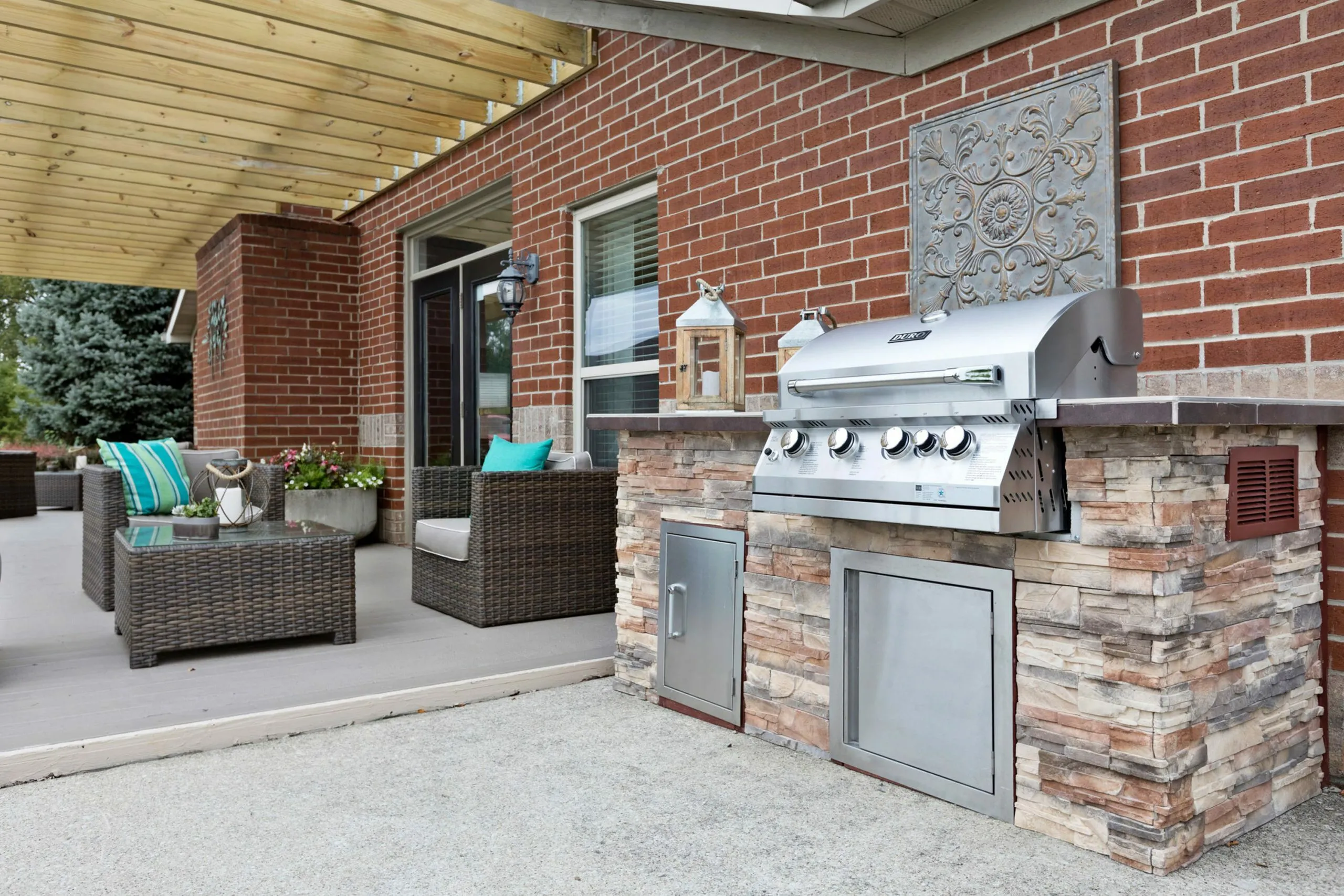 Charming backyard patio with stylish wicker furniture, vibrant turquoise cushions, and a sleek stainless steel grill under a wooden pergola.