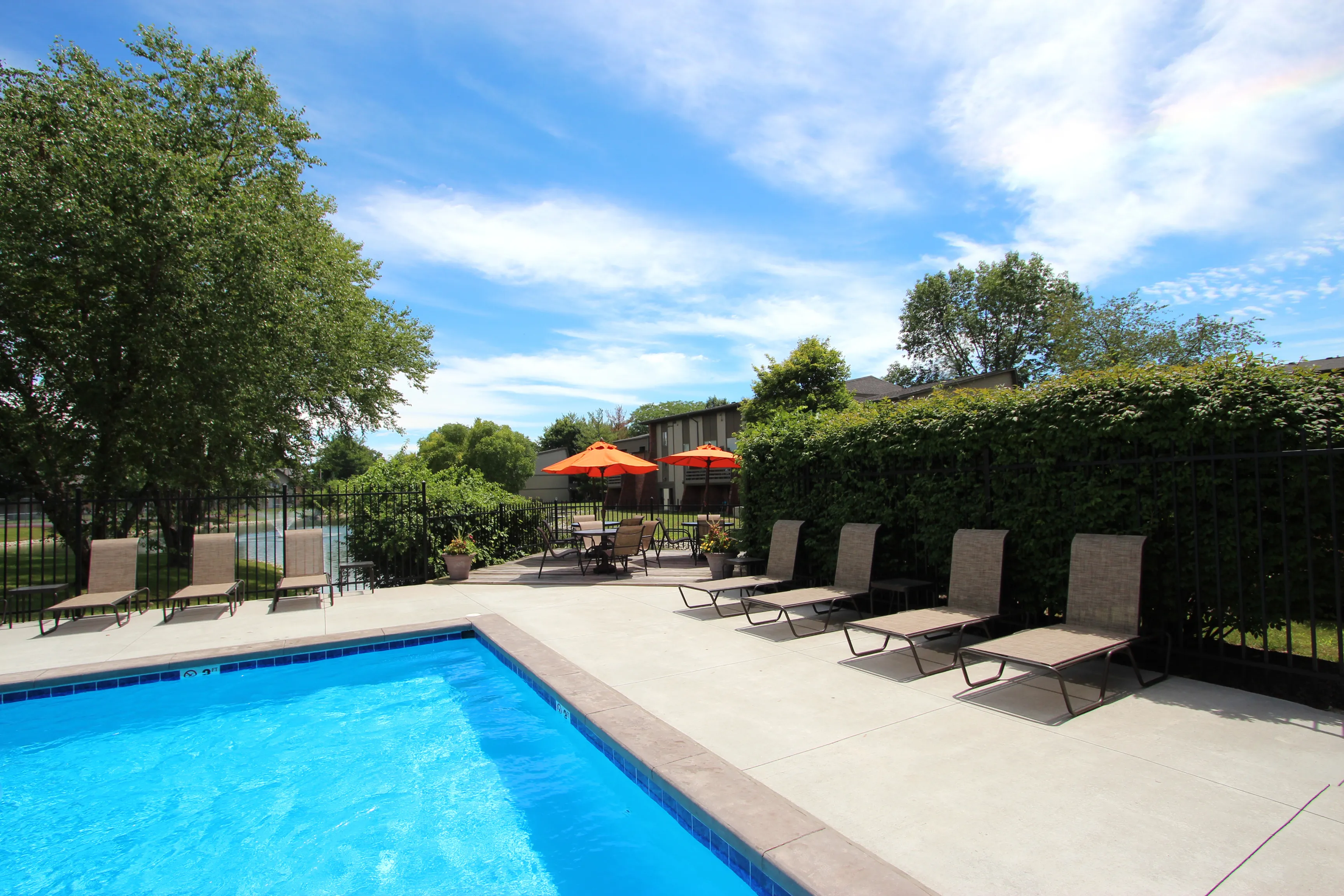 Inviting outdoor pool area with comfortable lounge chairs and vibrant orange umbrellas, perfect for relaxation under a clear blue sky.