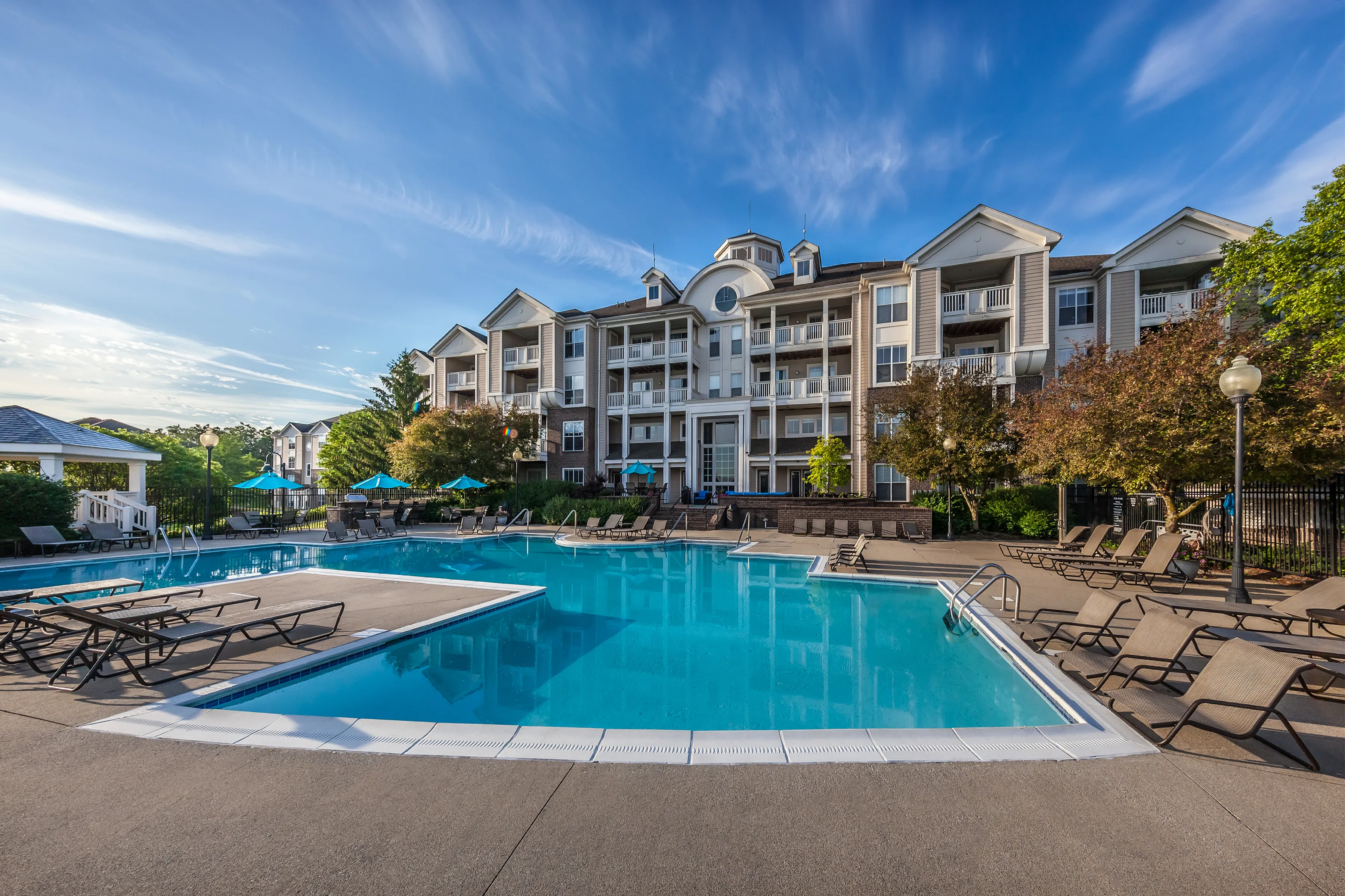 Luxury apartment community with a stunning pool area, surrounded by lush greenery and sun loungers, perfect for relaxation and leisure.