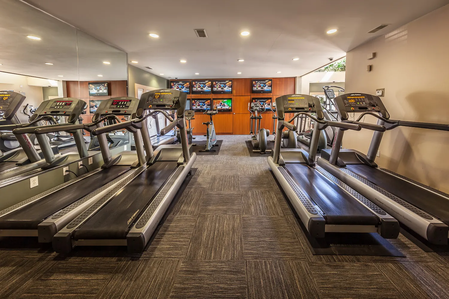 Modern fitness center with advanced treadmills, exercise bikes, and multiple TVs for an engaging workout experience.