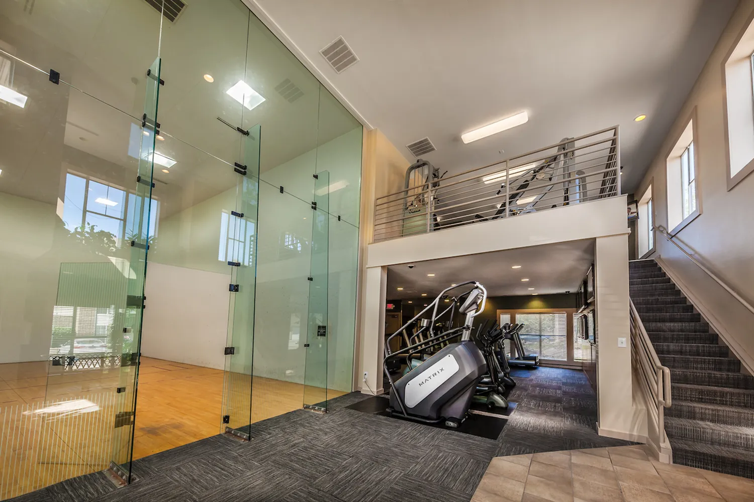 Modern fitness center featuring a glass-walled racquetball court, state-of-the-art exercise equipment, and an inviting mezzanine.