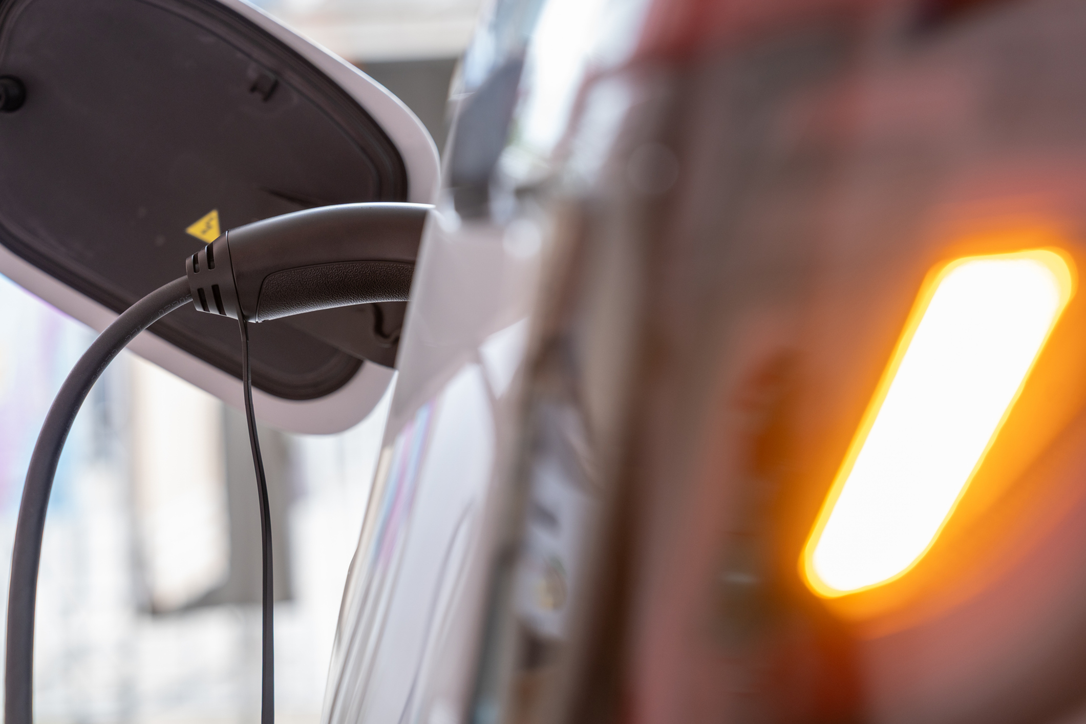 Close-up of an electric vehicle charging with a glowing indicator light, emphasizing eco-friendly technology and modern design.