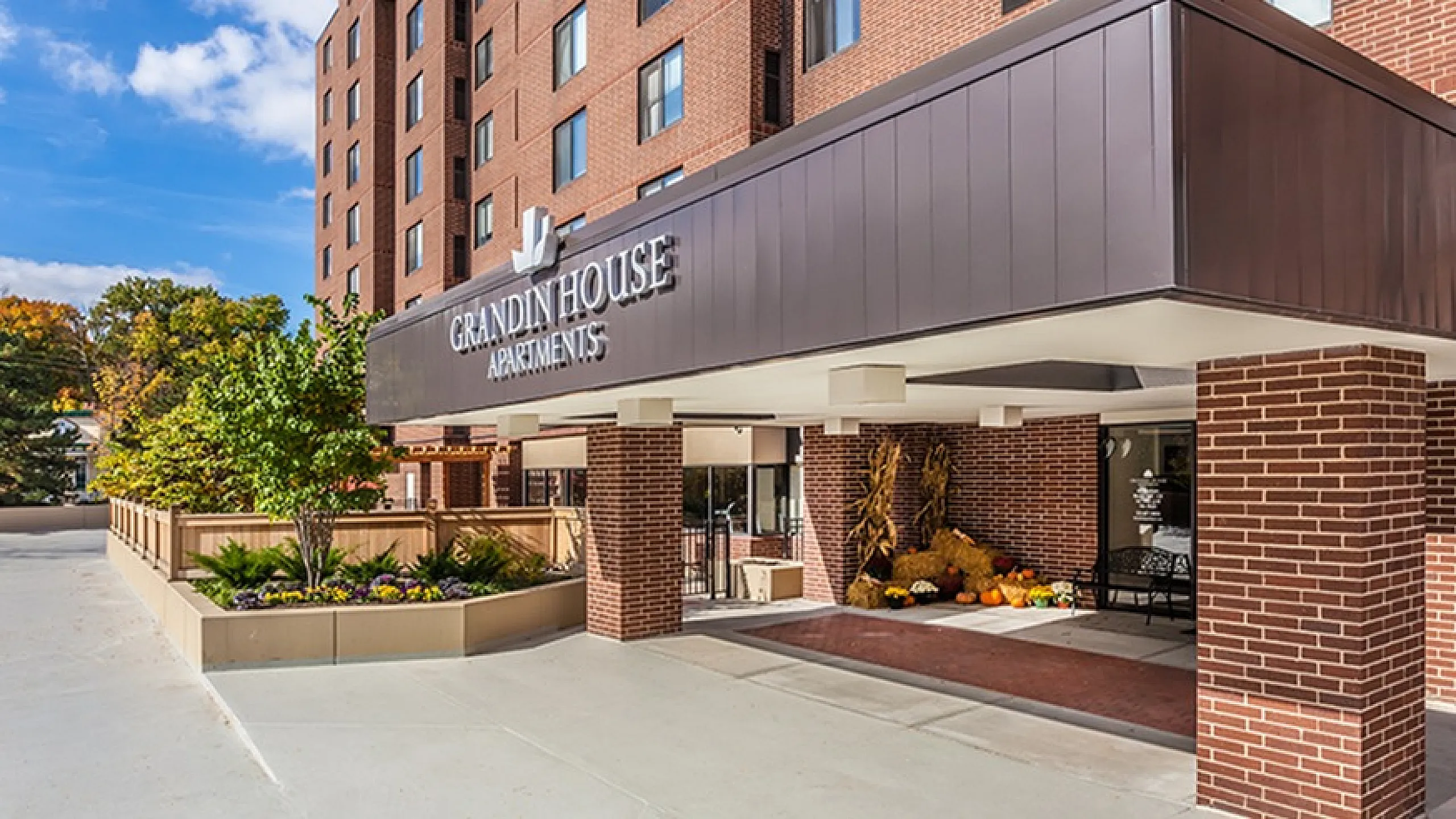 Elegant entrance of Grandin House Apartments with modern brick architecture, lush greenery, and welcoming decor.