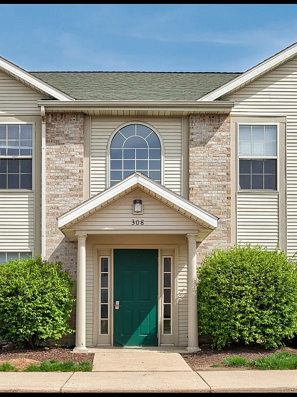 Charming colonial-style apartment exterior with elegant brick and siding facade, featuring stylish green front door and lush landscaping.