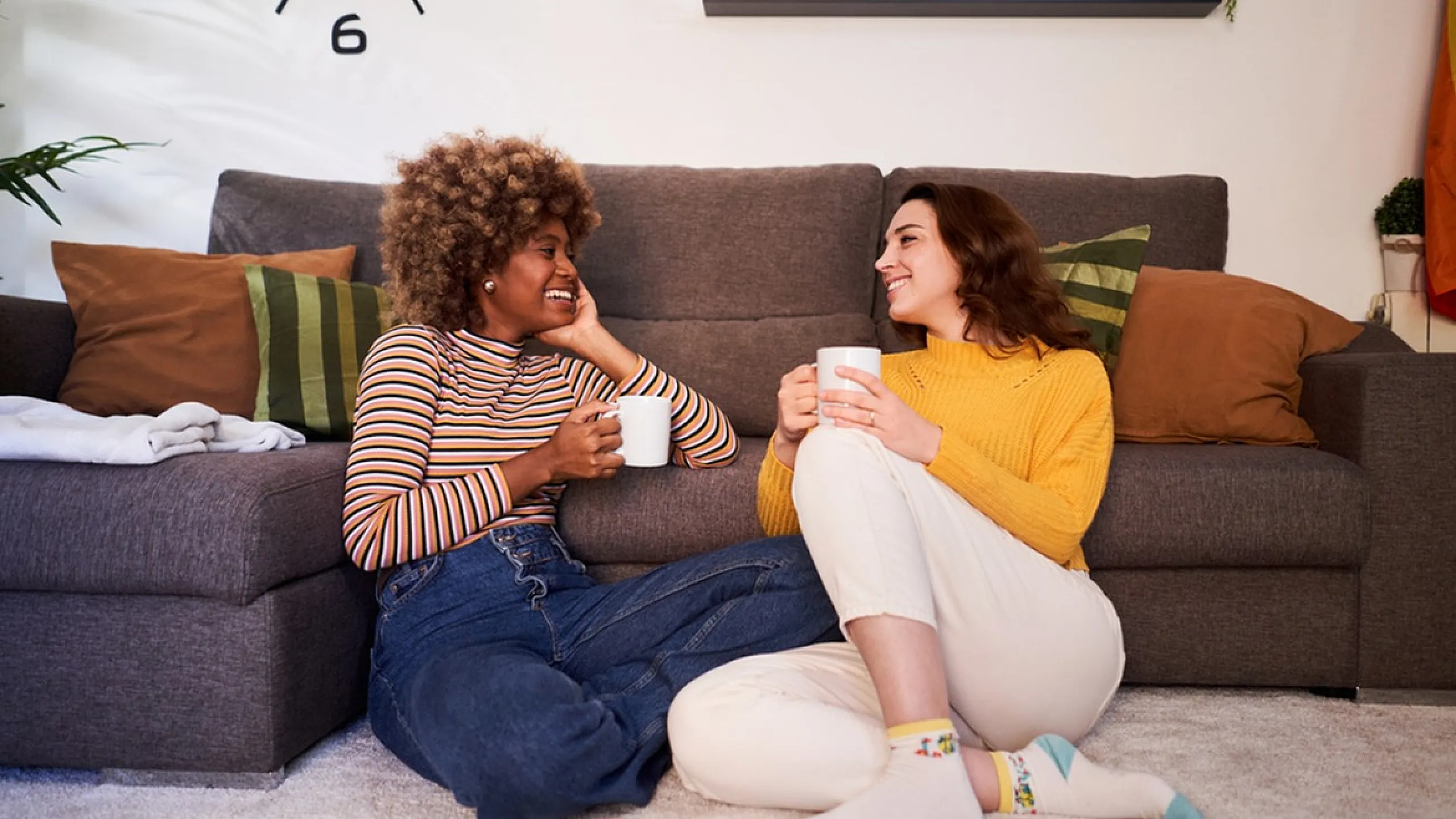 Cozy living room scene with two people enjoying coffee on a plush carpet next to a stylish sofa, vibrant pillows, and modern decor.