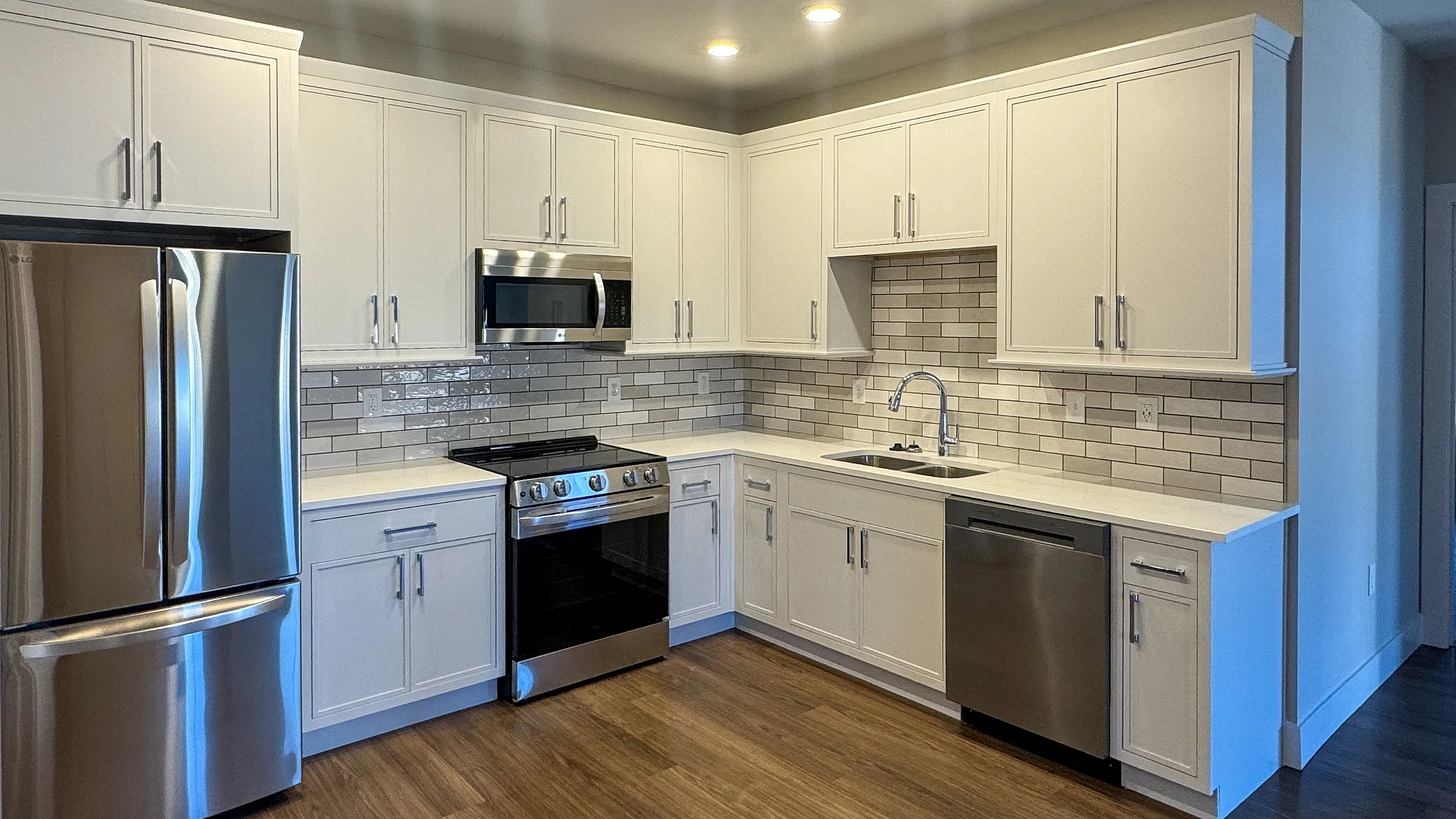 Modern kitchen featuring sleek stainless steel appliances, elegant white cabinetry, and a stylish tile backsplash, complemented by warm wood flooring.
