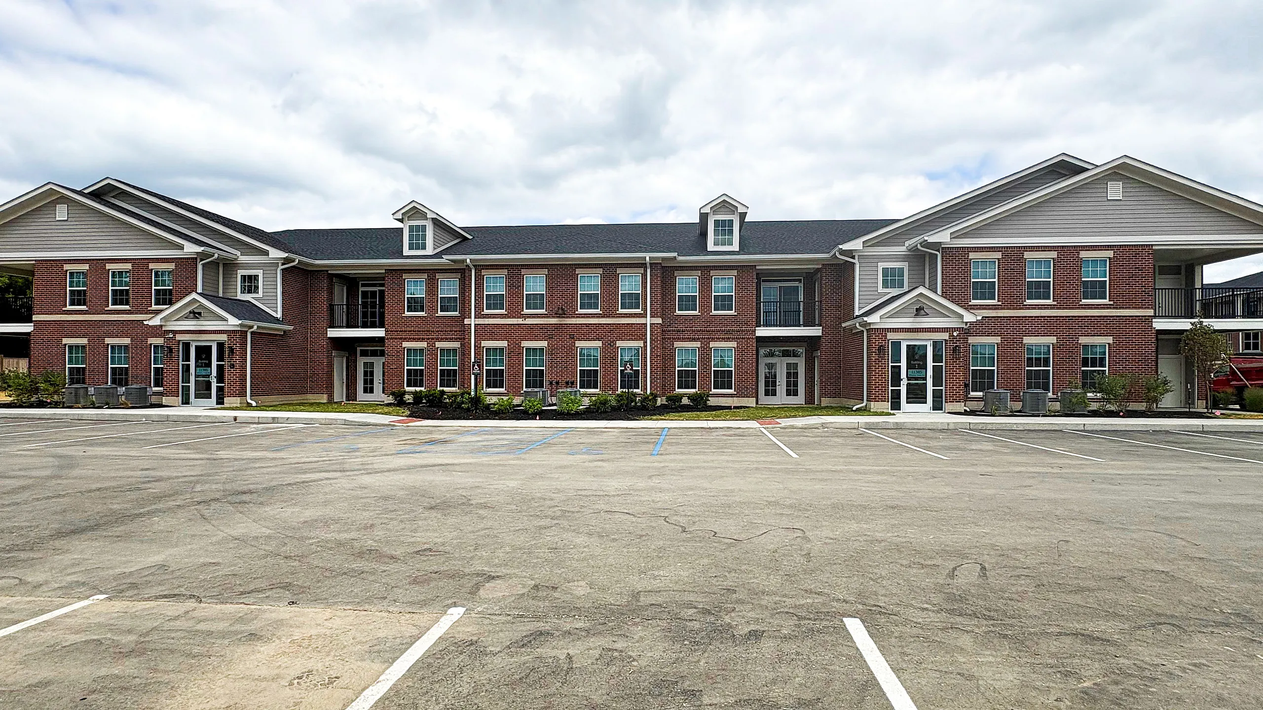 Elegant brick apartment complex with modern architecture and ample parking space.