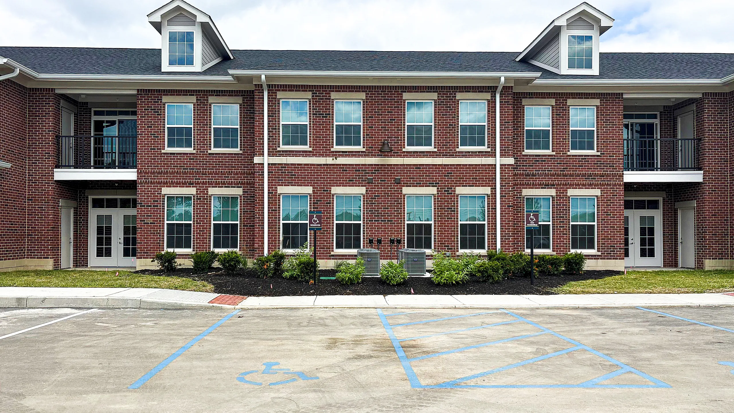 Elegant brick apartment building with classic colonial windows, lush landscaping, and accessible parking spaces.