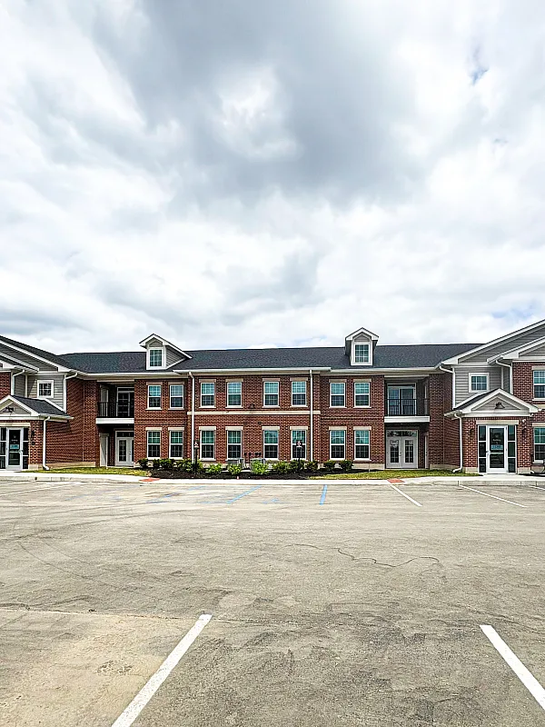 Charming brick apartment complex with modern design and spacious parking, set against a cloudy sky backdrop.