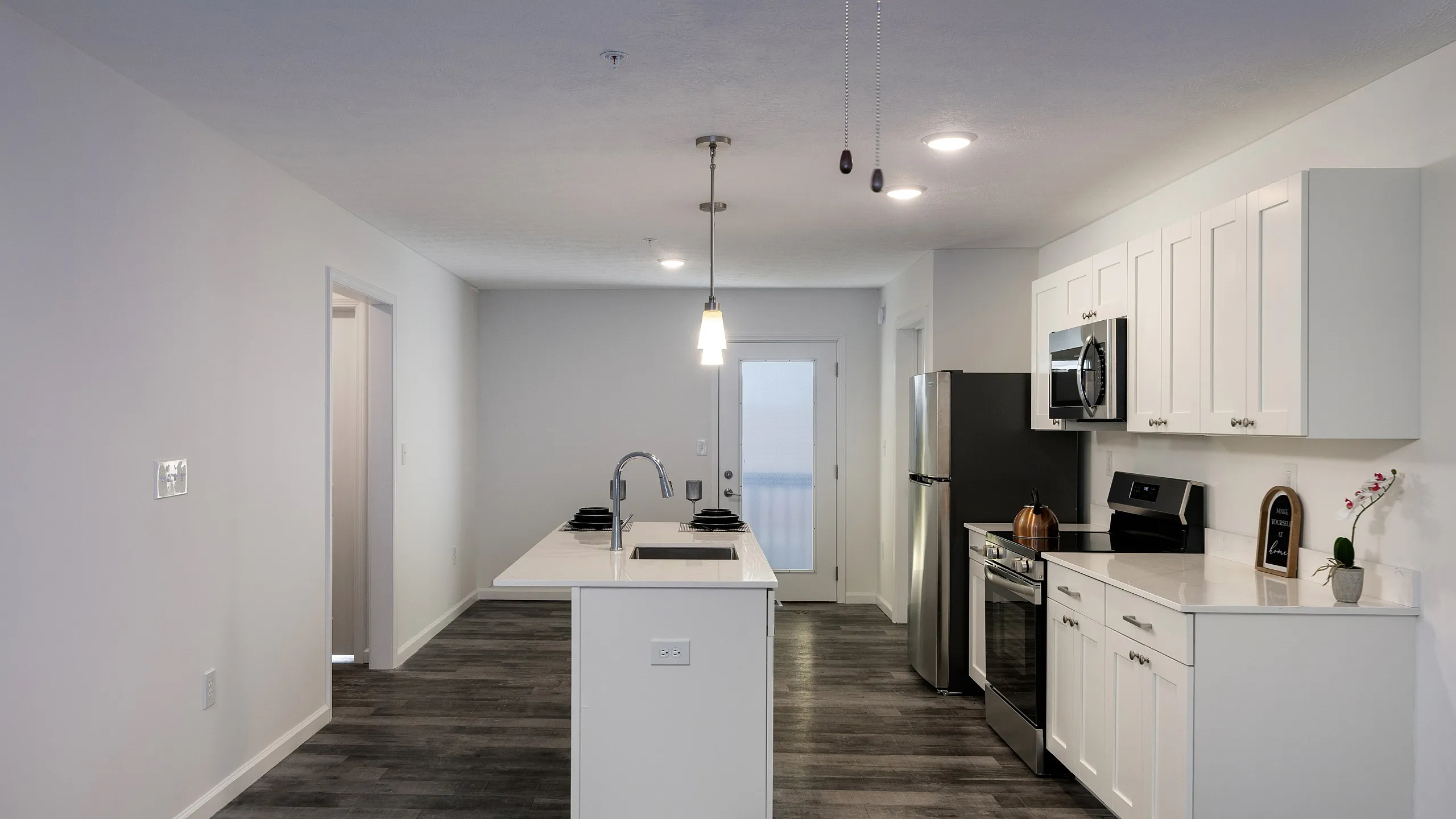 Modern kitchen with sleek white cabinets, central island, and stainless steel appliances under ambient lighting.
