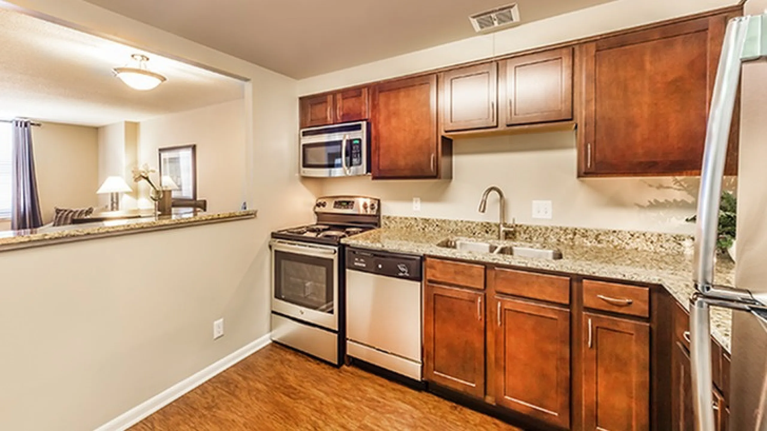 Modern kitchen with elegant wooden cabinetry, stainless steel appliances, and granite countertops adjacent to a cozy living area.