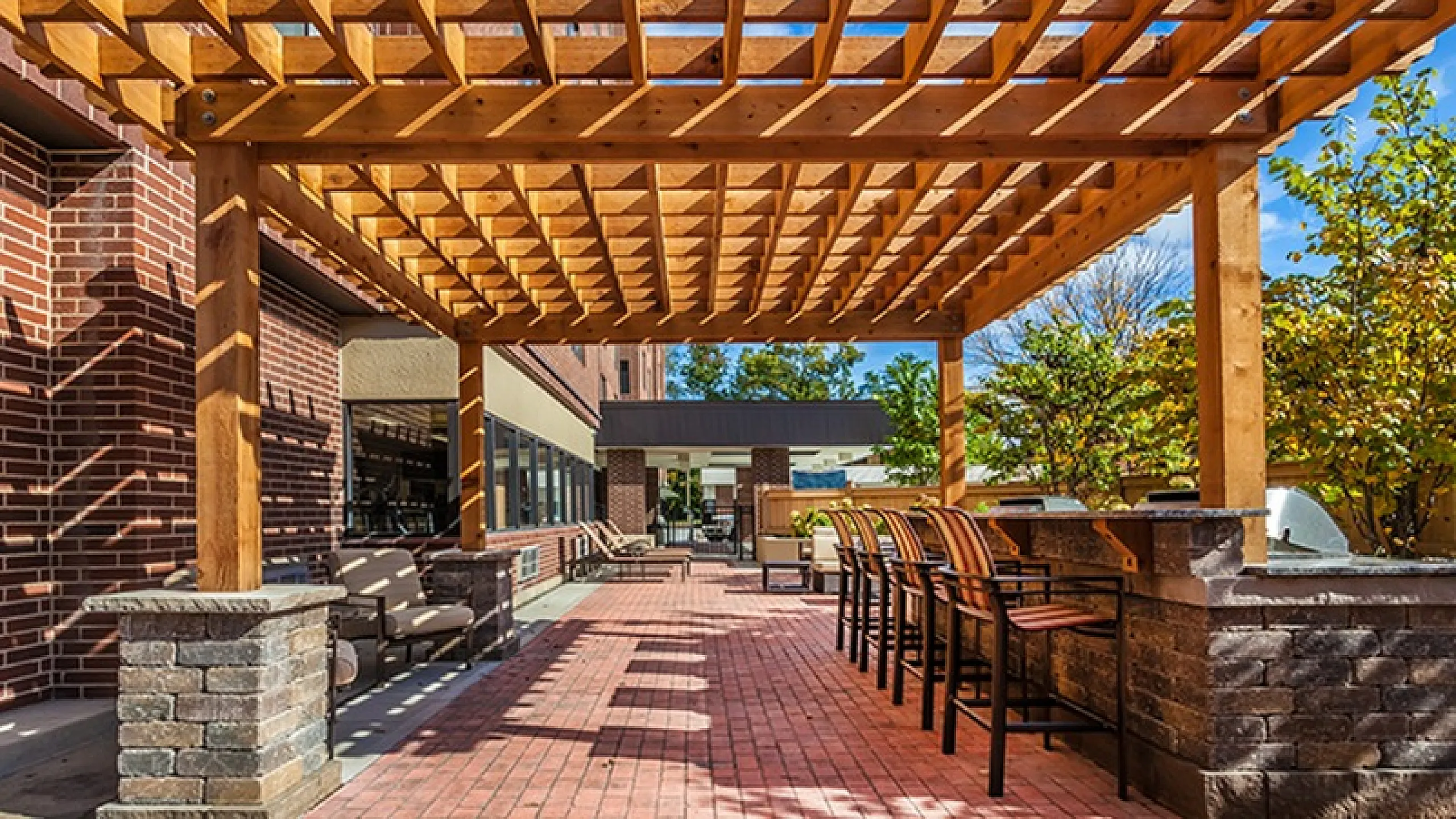 Charming outdoor patio with elegant wooden pergola, stylish brick columns, and inviting bar seating under a vibrant blue sky.