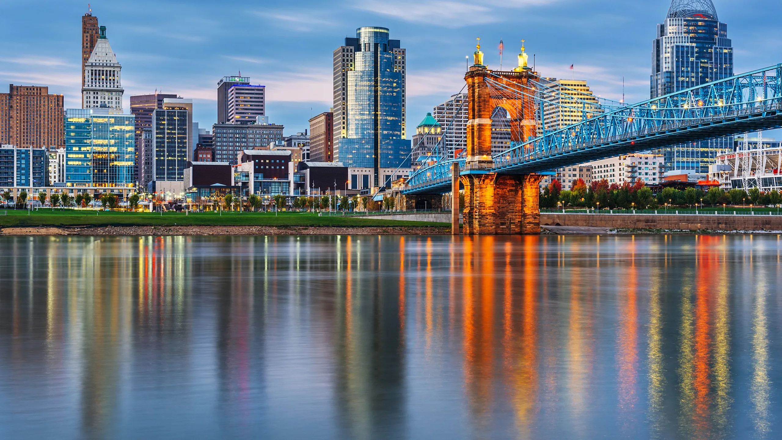 Vibrant cityscape with iconic bridge and modern skyline reflecting in serene river at dusk.