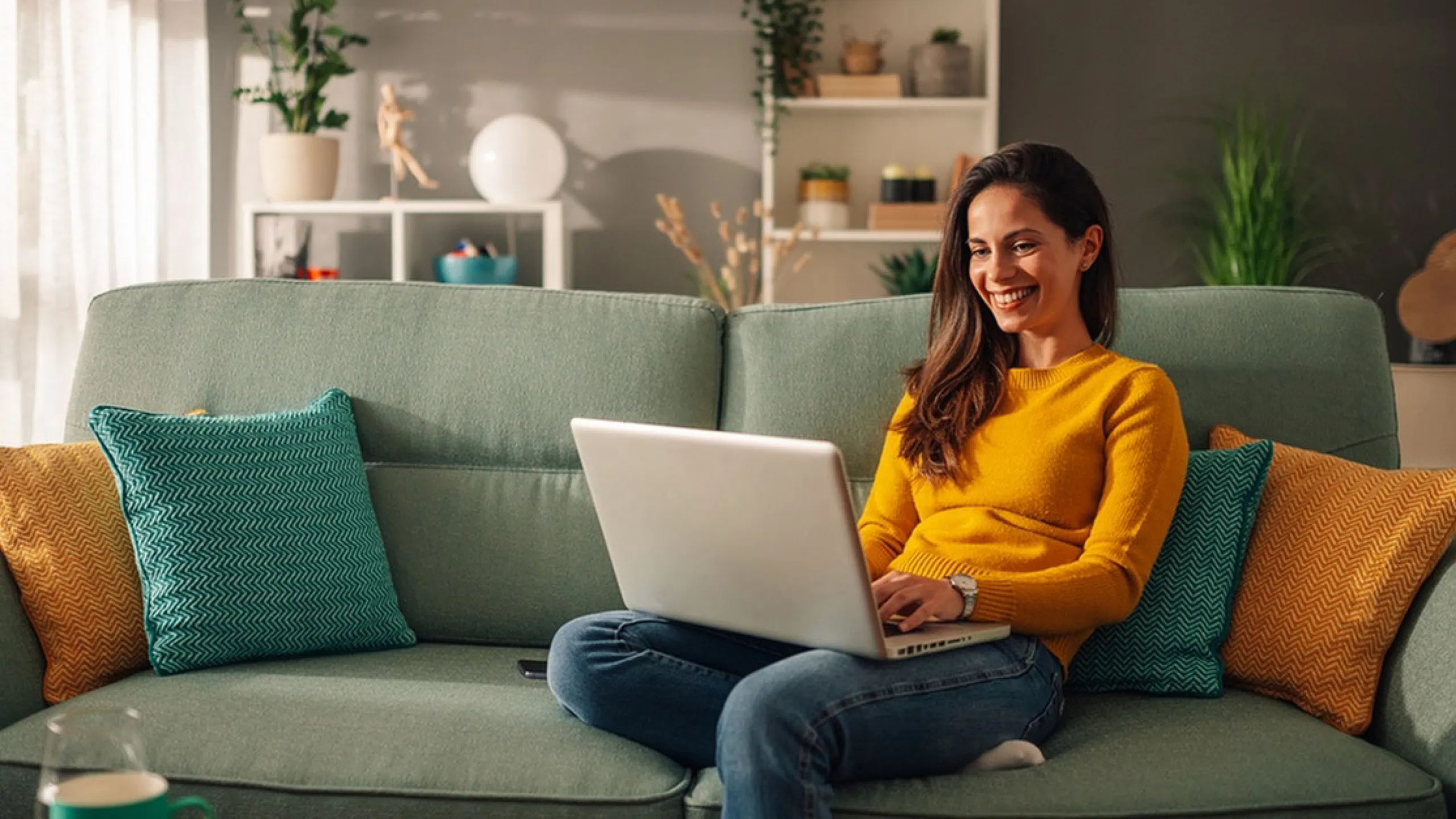 Cozy living room with a cheerful ambiance featuring a woman working on a laptop, surrounded by colorful cushions and vibrant green plants.