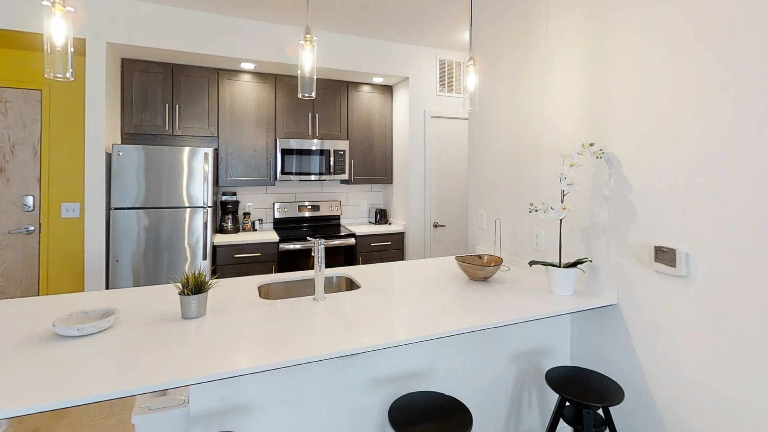 Modern kitchen with sleek stainless steel appliances, stylish pendant lighting, and a spacious white countertop with bar seating.