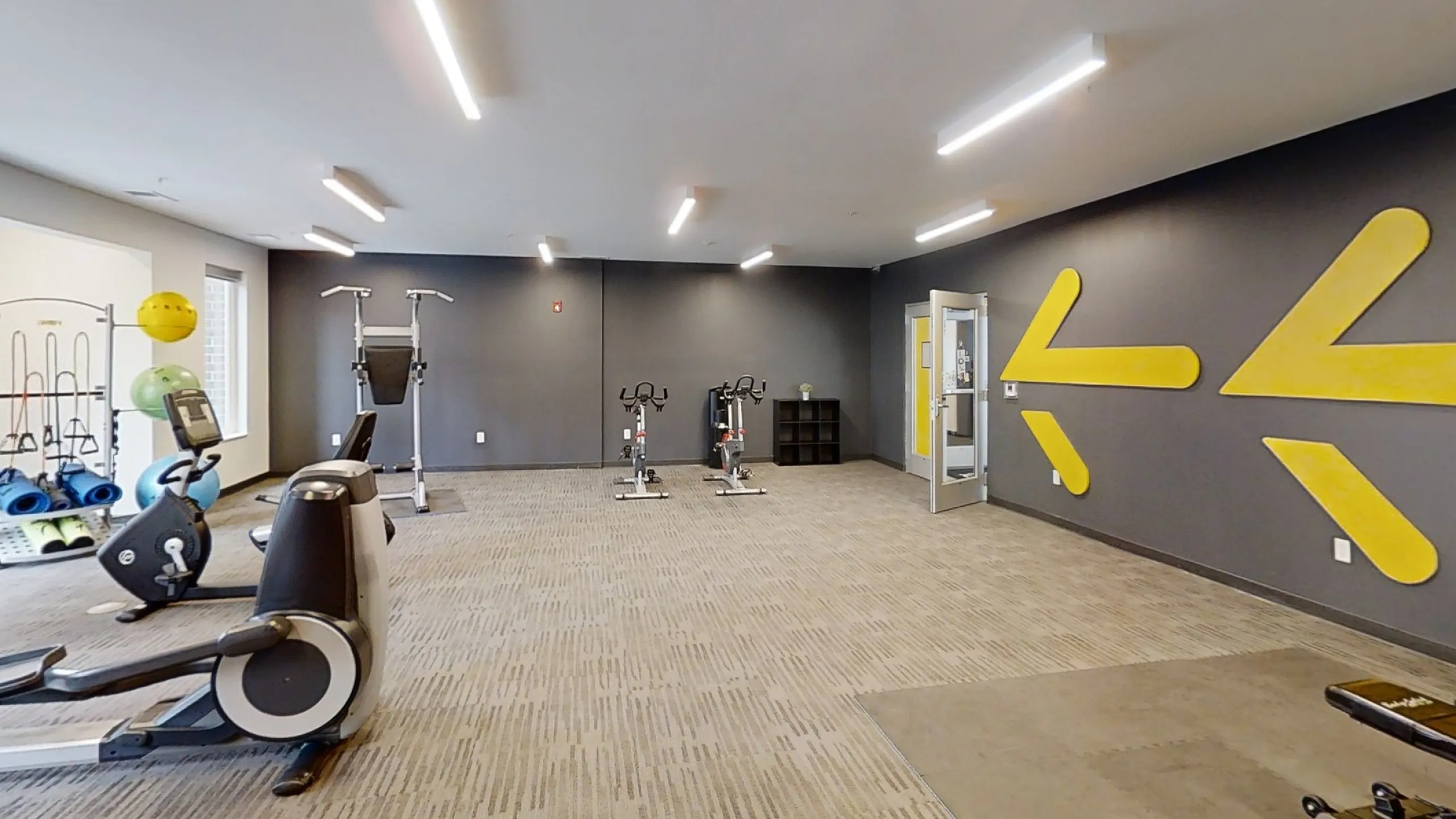 Spacious and modern gym with state-of-the-art exercise equipment, vibrant yellow accents, and ample natural light.
