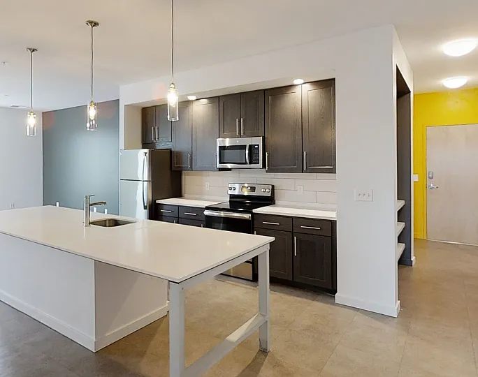 Modern open kitchen with sleek dark cabinets, a spacious island, and bright living area in a stylish apartment.