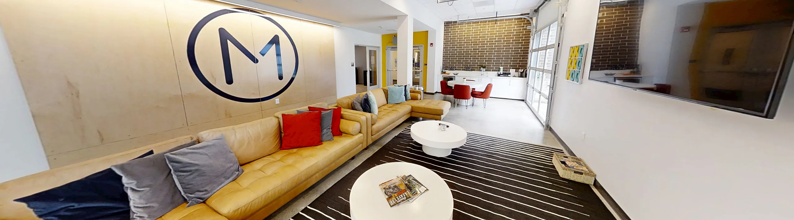Modern and spacious living area with stylish yellow sofas, decorative cushions, a sleek wall-mounted TV, and an open kitchen and dining space in the background.