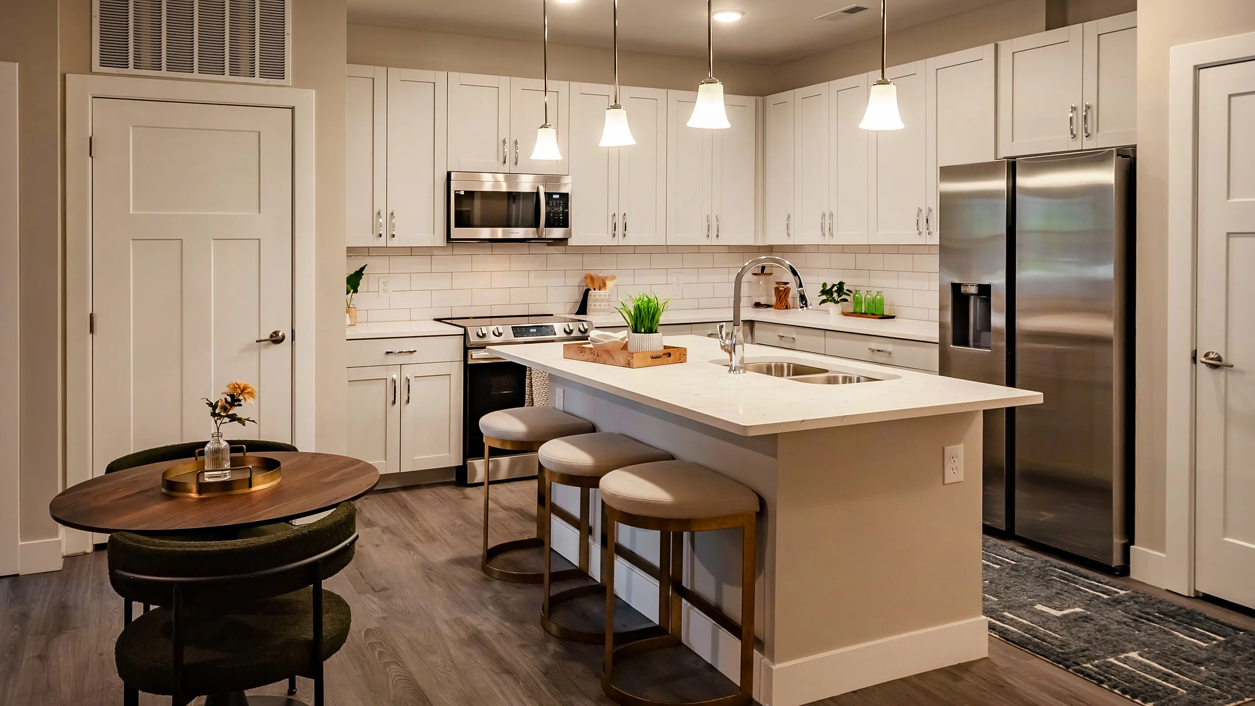 Modern kitchen with elegant lighting, white cabinetry, stainless steel appliances, and a cozy dining area.