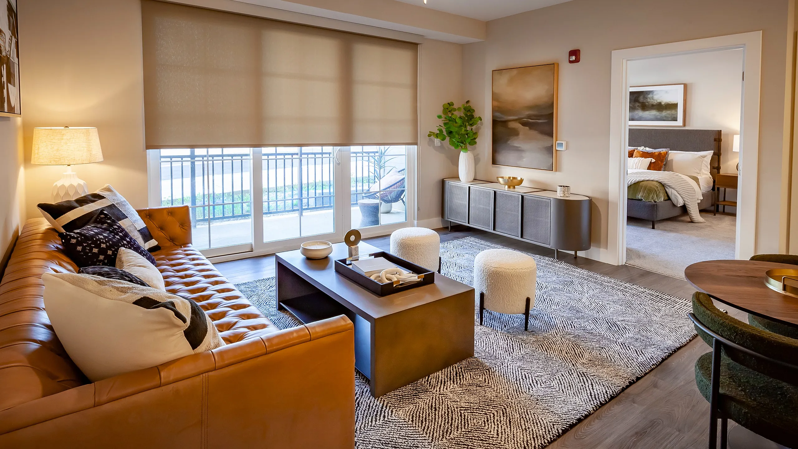 Elegant living room with a modern tan sofa, chic decor, and a view into the cozy bedroom, featuring stylish furnishings and abundant natural light.